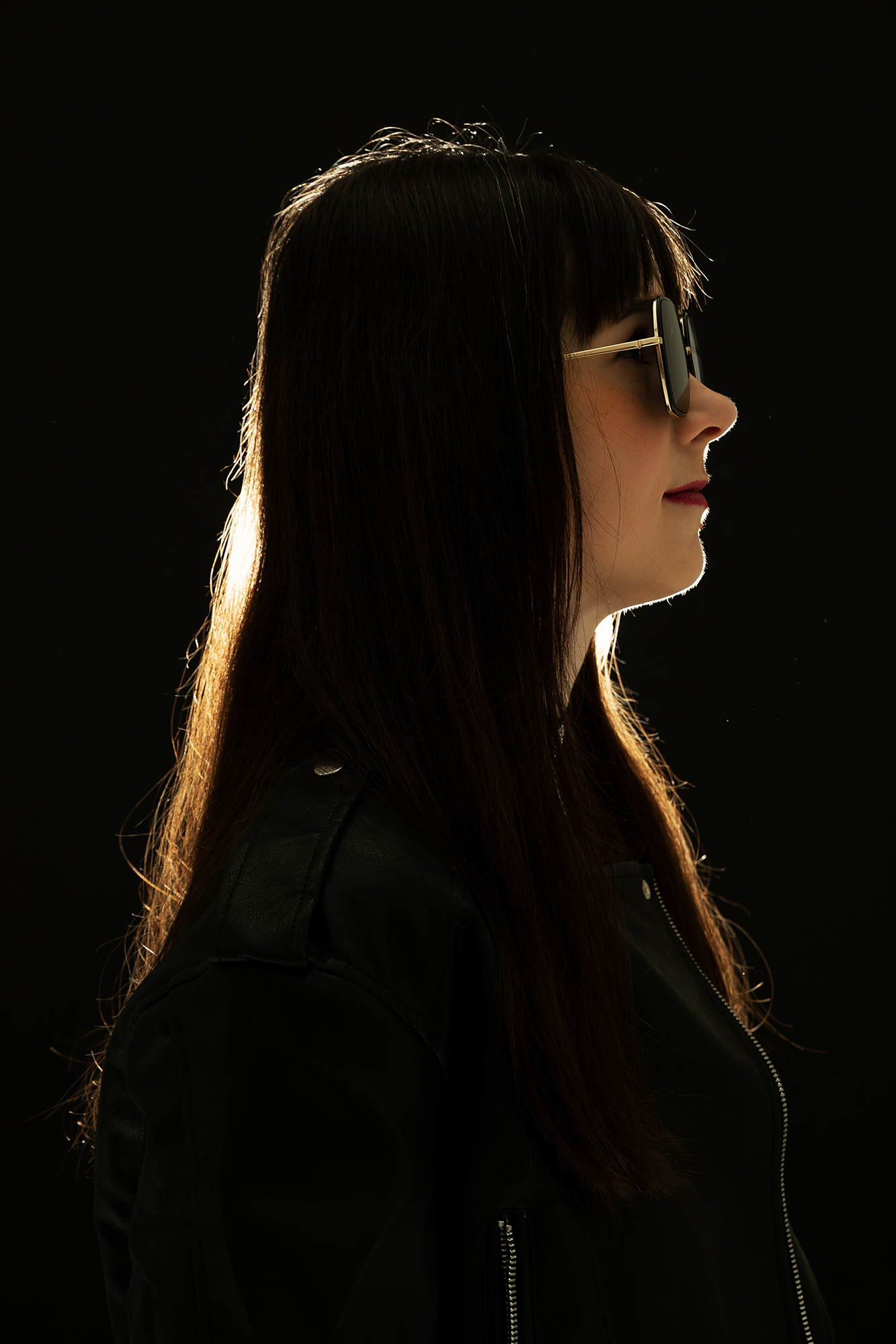 Rim-lit profile portrait of Aira Evard in sunglasses and a black leather jacket against a dark background