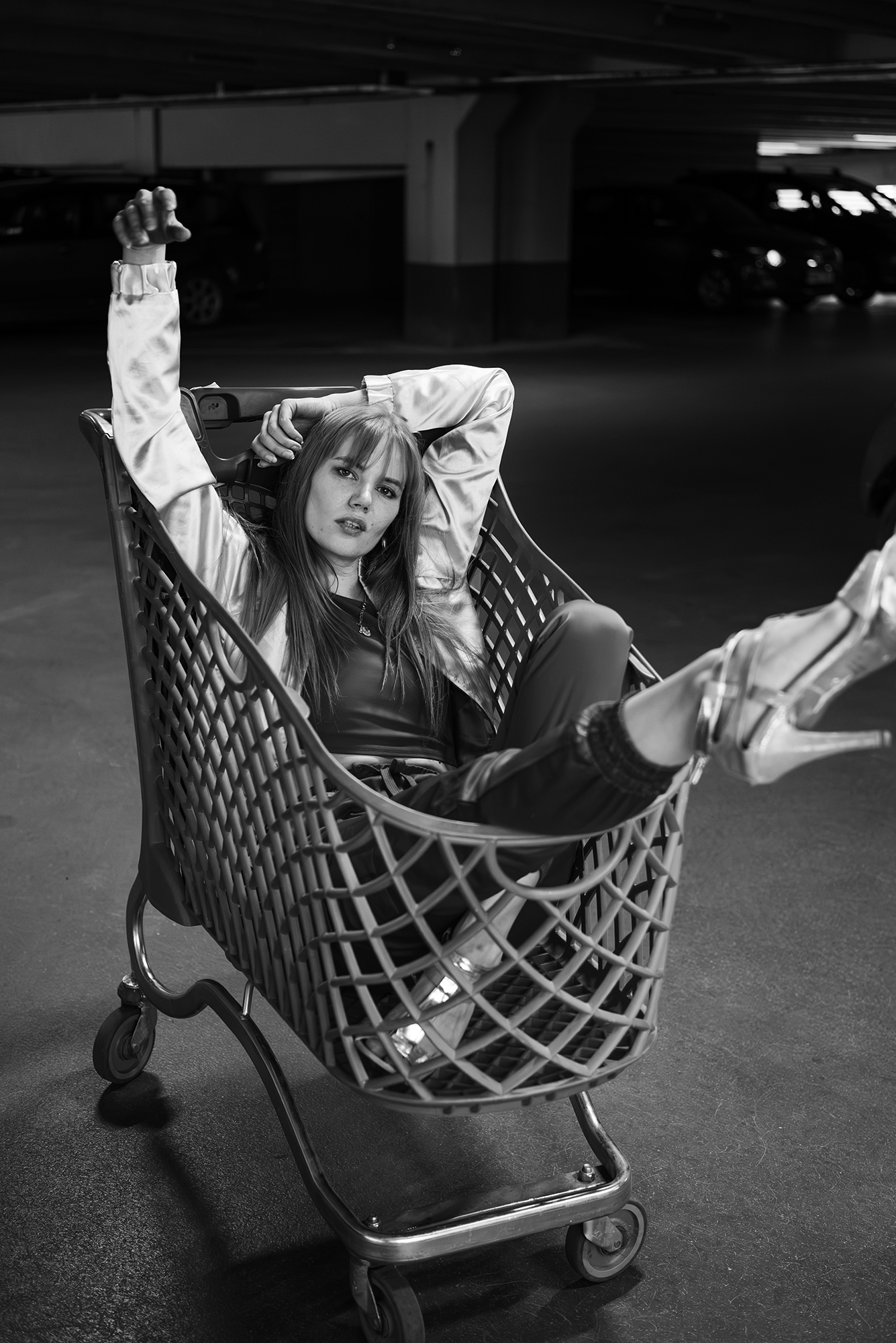 Black and white photograph of Helen Müürsep reclining inside a shopping trolley in an underground car park