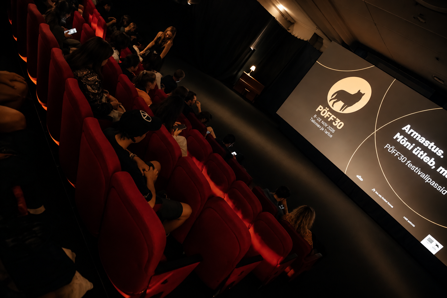 Festival audience seated in red cinema chairs facing the PÖFF30 screen