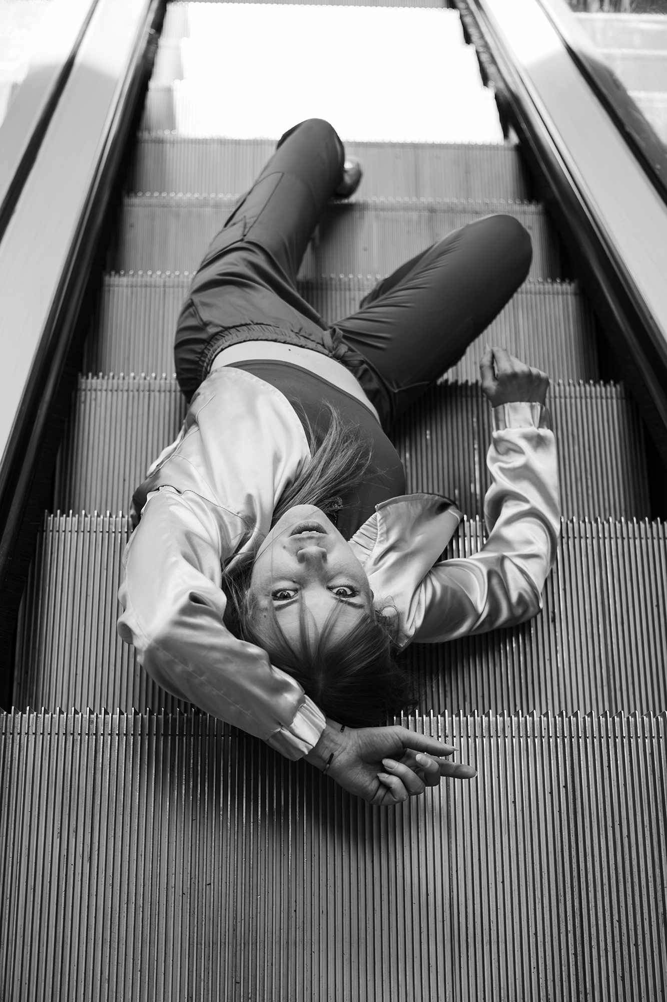 Black and white photograph of Helen Müürsep lying across escalator steps, arms above her head