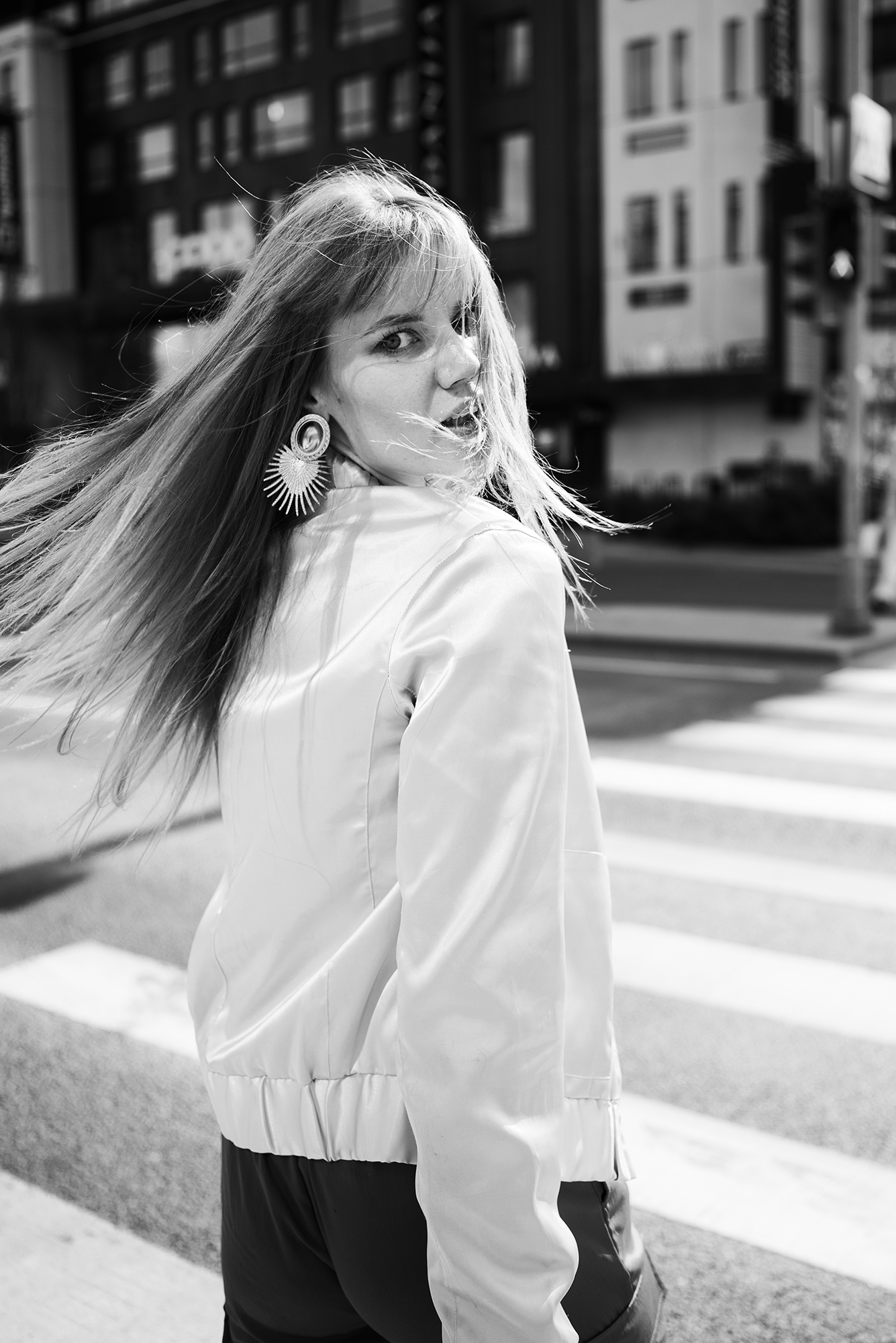 Black and white photograph of Helen Müürsep turning back towards the camera on a crosswalk, hair sweeping across the frame