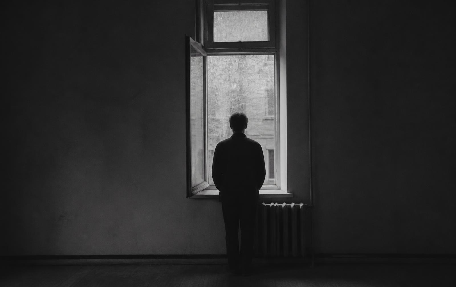 Lone figure at an open window in a bare room